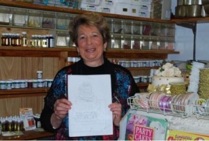Lorraine Kiewiet from Annie’s Cake Place holding a pencil drawing of the 175th birthday cake