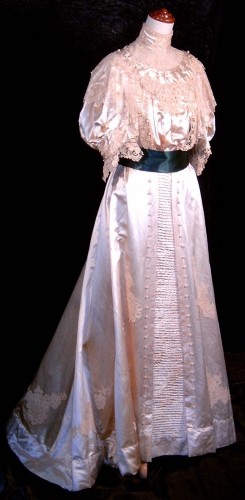 This gown was worn by a bride in Victoria in 1900.  It is of clotted cream slipper satin, the skirt with applied lace motifs, pintucking and passementerie baubles.  The bodice is decorated with brussels and guipure lace, again with passementerie baubles.  The sash was added when a second family bride wore the gown. From the Seams Old Australian Collection