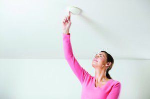 Young woman testing smoke alarm on ceiling